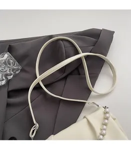 Gros plan du sac beige avec poignée en perles et fine bandoulière sur un costume