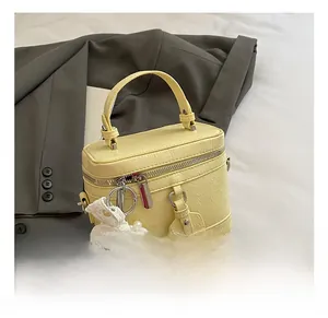 Close-up of a cream yellow leather bucket bag with lace pearl charm and gray blazer
