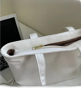 Close-up of golden metal zipper and white crocodile texture on oversized tote bag