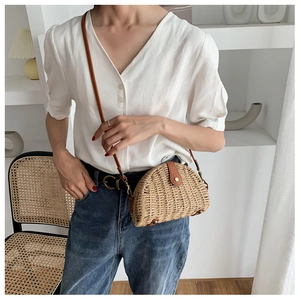 Detail of handwoven semi-circle straw bag with brown leather flap and gold metal buckle