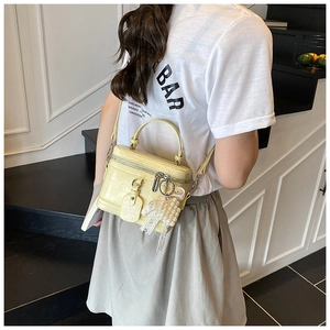 Detail of light yellow box bucket bag featuring pearl lace charm and smooth leather folds