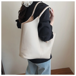 Close-up of ivory bucket bag showing asymmetrical curved opening and litchi texture leather