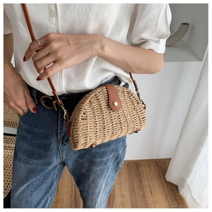Detail of semicircular straw crossbody bag with brown leather strap and metal bottom studs