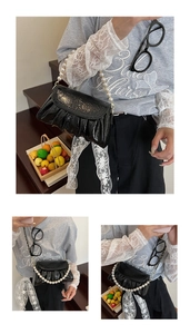 Détail du sac froncé en cuir verni noir avec bandoulière perle et chaîne métal