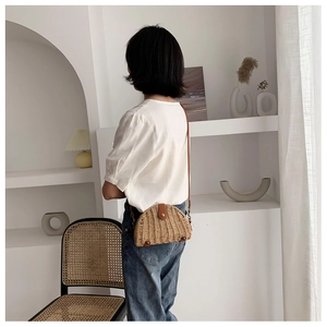 Detail of a semi-circular straw crossbody bag with brown leather strap on a model