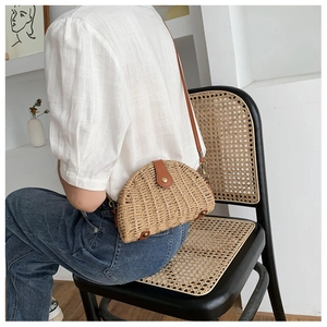 Detail of a semi-circular straw bag with brown leather trim and metal clasp for summer