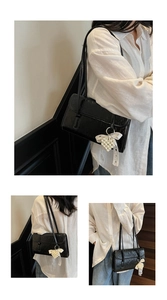 Detail of black glossy shoulder bag featuring pearl heart charm and elegant white ribbon