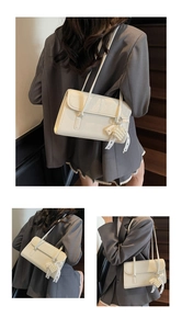 Detail view of cream shoulder bag with pearl heart charm and lace bow on a textured leather flap