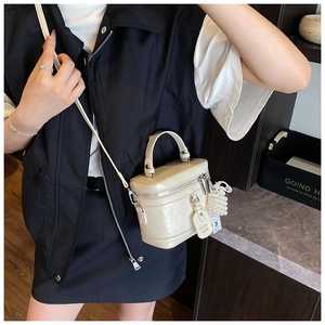 Detail view of beige glossy patent leather handbag with pearl charm and metal zipper