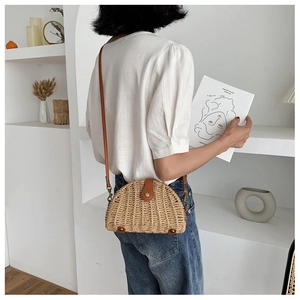 Detailed view of the semi-circular straw crossbody bag with brown leather strap and metal clasp