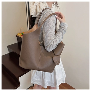 Close-up of a large dark brown lychee leather bucket bag with curved rim on a model