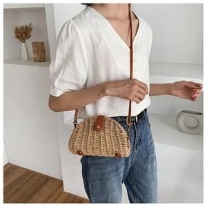Detail of a semicircular straw crossbody bag with brown leather strap on a model