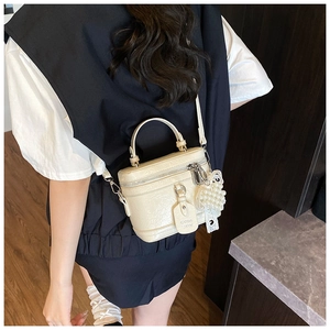 Detail view of cream textured leather handbag with pearl charm and metal zipper