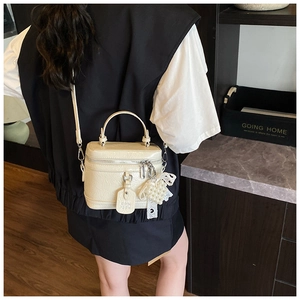 Close-up of off-white crossbody bag with pearl lace charm and pleated texture detail