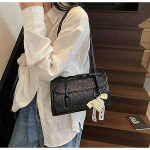 Detail of black pleated faux leather underarm bag with pearl heart and lace bow