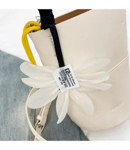 Detail view of beige leather bucket bag featuring white fabric flower charm and yellow cords