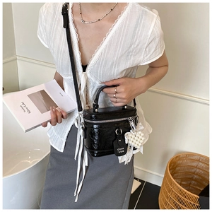 Close-up of a black pleated leather handbag with pearl heart charm and metallic zipper