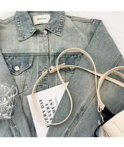 Detail of a creamy white leather crossbody bag with adjustable strap on denim jacket
