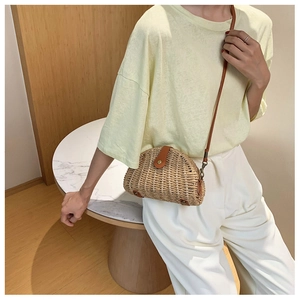 Close-up of semi-circular straw woven crossbody bag with brown leather details