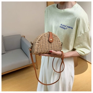 Close-up of semi-circle straw saddle bag with hand-woven texture and leather strap detail