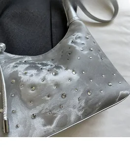 Detail showing shiny silver pleated fabric and sparkling rhinestone accents on the handbag