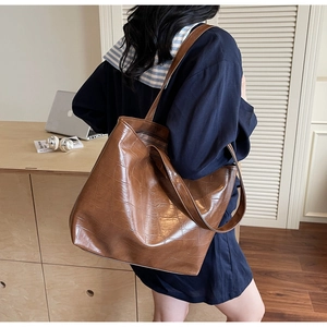 Detail of a large brown crocodile-patterned tote bag with polished finish and long shoulder strap
