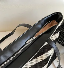 Detail of smooth metal zipper and black leather trim on a striped woven tote bag