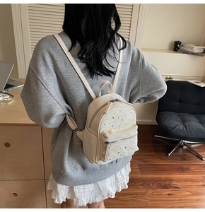 Back view of a mini beige quilted backpack with rhinestone studs on a gray sweatshirt
