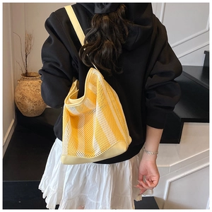 Detail of yellow striped mesh tote bag with leather straps on model in stylish interior