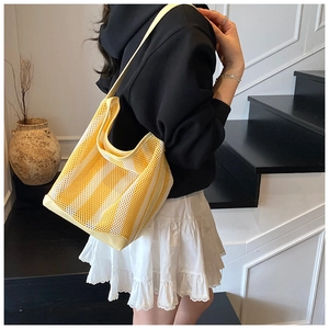 Detail of yellow and white striped mesh tote bag worn on shoulder by a model