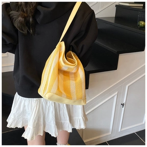 Détail du sac cabas en maille à rayures jaunes et blanches porté à l'épaule, style épuré