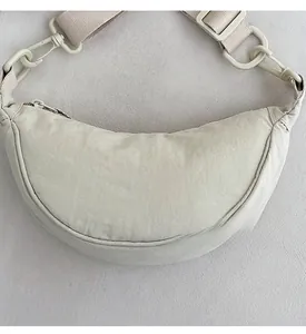 Detail view of cream nylon crescent bag showing adjustable wide strap and plastic hardware