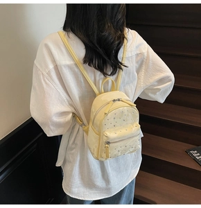 Mini yellow backpack with rhinestones shown on model back against wooden stairs