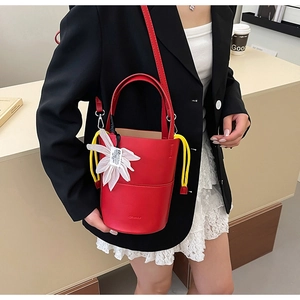 Detail of red leather bucket bag with white floral charm and yellow drawstring