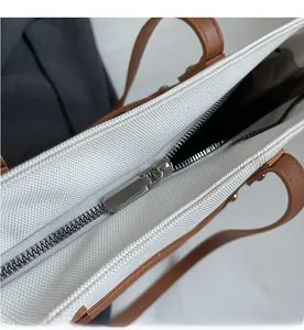 Macro detail of high-quality smooth silver zipper on a beige canvas tote bag with brown trim