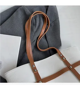 Close-up of contrast color tote bag with brown leather handles and metal rivet details