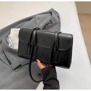 Detailed view of black pleated leather shoulder bag on a grey blazer background