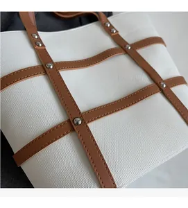 Detailed view of woven canvas tote featuring brown leather straps and silver metal rivets