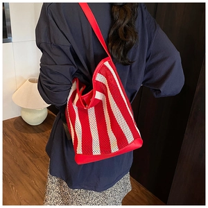 Détail d'un sac seau en maille à rayures rouges et blanches porté à l'épaule