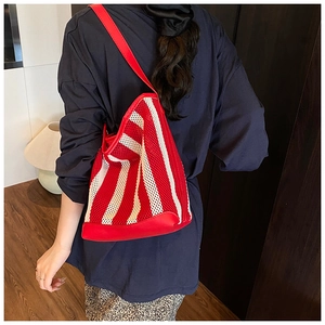 Detail of red striped hollow mesh tote bag with leather strap on model shoulder