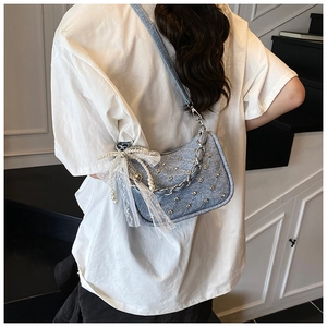 Détail du sac en denim bleu clair avec clous argentés, nœud en dentelle et perles