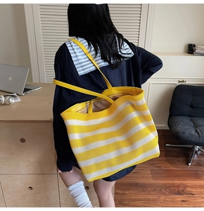 Detail of a large yellow and white striped mesh tote bag worn on shoulder in a home office