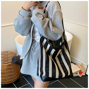 Detail of black and white striped mesh tote bag worn on shoulder in a minimalist room