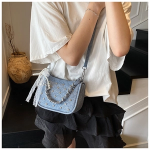 Détail du sac bandoulière en denim bleu clair avec clous et nœud en dentelle