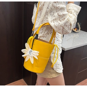 Detail of a bright yellow leather bucket bag with a 3D white flower charm for women