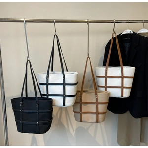 Detail of multi-color tote bags with cross-stitch straps and metallic rivets on a rack