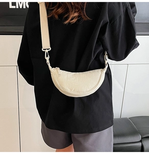 Detail of off-white nylon crescent crossbody bag with wide shoulder strap worn on person