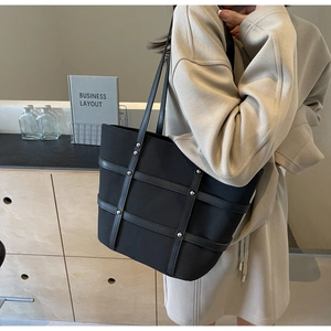 Detail of black tote bag featuring woven leather straps and metal rivet accents