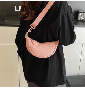 Pink nylon crescent crossbody bag with adjustable strap worn by model in a minimal setting