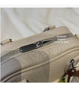 Close-up of smooth silver metal zipper and lychee pattern leather on beige handbag